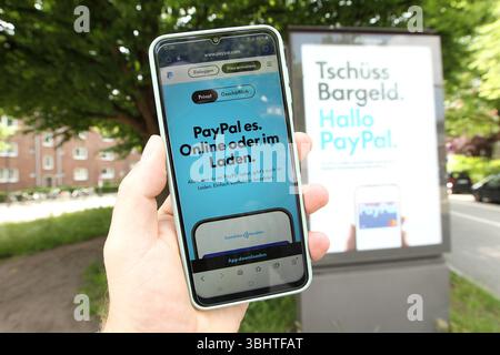 Anti-Bargeld-Werbung auf einer Werbetafel von Ströer vom Online-Bezahldienst PayPal. DAS Unternehmen wirbt aktuell in Deutschland großspurig für die Möglichkeit, mit seiner App kontaklos zu zahlen. Davor hält ein Mann ein smartphone in der hand, auf dem die website von PayPal geöffnet ist. Dort informiert das Unternehmen über die Möglichkeit des kontaklosen Zahlens. Barmbek Hambourg *** publicité anti-cash sur un panneau d'affichage Ströer du service de paiement en ligne PayPal la société annonce actuellement la possibilité de payer sans contact avec son application en Allemagne dans le grand style devant Banque D'Images