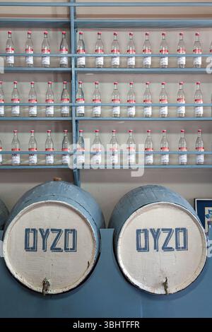 Intérieur d'une distillerie grecque traditionnelle avec des rangées de bouteilles d'ouzo et des tonneaux vieillissants, mettant en valeur l'artisanat local et le patrimoine. Banque D'Images