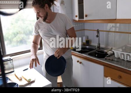 Homme préparant les ingrédients et ramassant l'assiette dans la cuisine Banque D'Images
