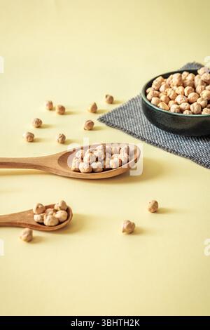 Composition minimaliste avec des pois chiches dans des cuillères en bois et bol en céramique sur fond pastel chaud. Concept alimentaire sain et naturel Banque D'Images