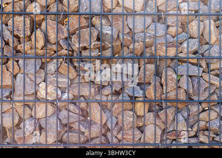Une vue détaillée d'un mur fait de roches de forme irrégulière fixées à l'intérieur d'une grille métallique noire. Les pierres varient en taille et en couleur, créant un organique Banque D'Images