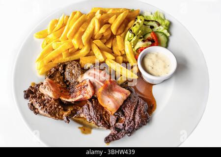 2 steaks tranchés avec bacon frit, frites, légumes et laitue, sauce sur assiette blanche, gros plan. Banque D'Images