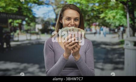 Femme tenant des billets de banque zloty polonais dans une rue de la ville, entourée de paysages extérieurs, communique un sentiment d'assurance financière et de lif urbain décontracté Banque D'Images