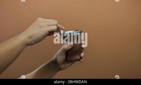 Homme préparant la boisson traditionnelle de maté en utilisant une gourde en cuir brun sur un fond de mur isolé. Banque D'Images