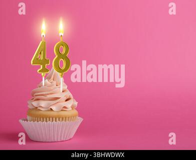Délicieux cupcake avec des bougies en forme de nombre brûlant sur fond rose, espace pour le texte. 48e anniversaire ou autre occasion spéciale Banque D'Images