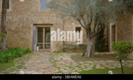 Vue floue sur une ancienne maison méditerranéenne en pierre avec un effet bokeh, avec un cadre extérieur rustique avec des arbres et de la verdure au premier plan. Banque D'Images