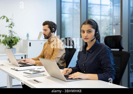 Une femme et un homme travaillant dans un centre d'appels. Tous deux portent des casques et travaillent sur des ordinateurs portables. Banque D'Images