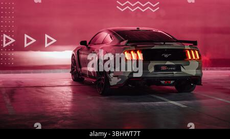 Camo beige Ford Mustang dans le garage de stationnement. Vue arrière de trois quarts d'un poney américain garé près d'un mur marron éclairé. Banque D'Images
