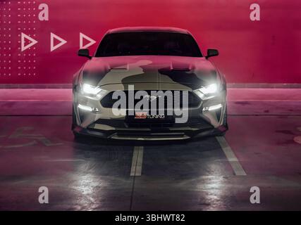 Camo beige Ford Mustang dans le garage de stationnement. Vue avant du poney car américain garé près du mur rouge illuminé. Banque D'Images