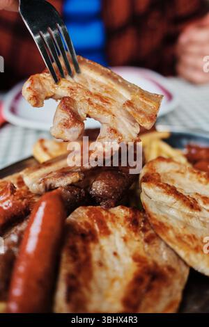 Fourchette tenant un morceau de viande grillée juteux d'un plat de gril serbe traditionnel. Fermer la vue. Cuisine balkanique. Banque D'Images