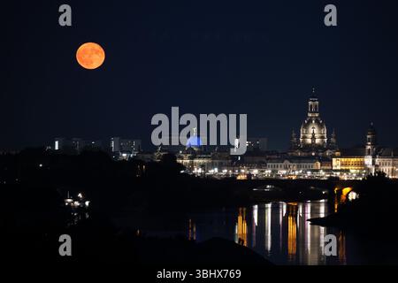 Dresde, Allemagne. 11 juin 2025. Les passants regardent la lune à la fraise se lever sur les rives de l'Elbe avec pour toile de fond la vieille ville. Crédit : Sebastian Kahnert/dpa/Alamy Live News Banque D'Images