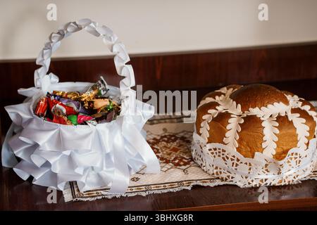 Une nature morte magnifiquement arrangée présente un pain de Pâques rond orné de dentelle blanche et un panier rempli de bonbons au chocolat colorés, presente Banque D'Images