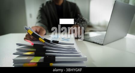 Un bureau de travail de personne de transformation numérique avec ordinateur portable et grande pile de documents, stylo de maintien, environnement de bureau moderne, avec la paperasse de focus Banque D'Images