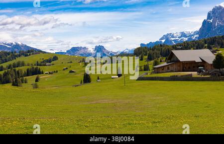 Une cabane de montagne traditionnelle en bois nichée dans de vastes prairies verdoyantes de l'Alpe di Siusi, avec les majestueux sommets enneigés des Dolomites sous une bri Banque D'Images