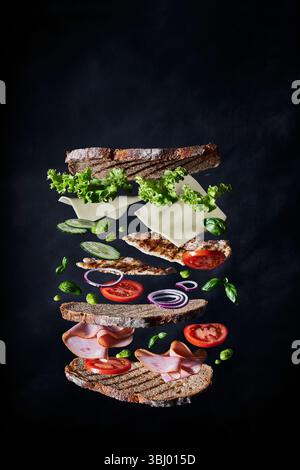 Un sandwich déconstruit avec des ingrédients flottants comprenant du pain rustique, de la laitue, du fromage, de la tomate, du concombre, et la turquie, sur fond sombre, highli Banque D'Images