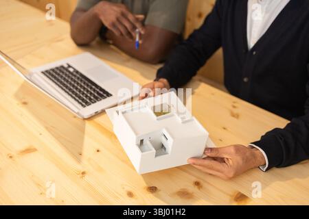 Une réunion collaborative dans un espace de coworking moderne à Barcelone. Deux personnes discutent sur un ordinateur portable et examinent un modèle architectural 3D sur un bois Banque D'Images