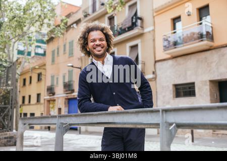 Un homme profite d'un moment de détente en dehors d'un espace de coworking à Barcelone. Il se penche sur une balustrade, entouré de charmants vieux bâtiments et d'arbres Banque D'Images