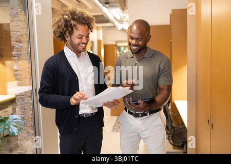 Deux professionnels divers participent à une discussion dans un espace de coworking dynamique à Barcelone, partageant des idées avec des documents et une tablette numérique dans un mod Banque D'Images
