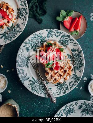 De délicieuses gaufres garnies de fraises fraîches et de crème fraîches sont élégamment servies sur de belles assiettes à motifs floraux, créant un an visuellement attrayant Banque D'Images