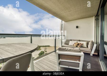 Un balcon élégant avec un coin salon confortable donnant sur une vue sur l'eau sereine et le ciel lumineux, idéal pour la détente et les loisirs Banque D'Images