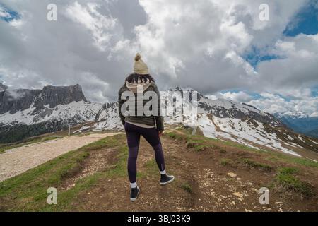 Une femme se tient à Passo Giau dans les Dolomites, en Italie, regardant les montagnes enneigées sous des nuages spectaculaires. Les paysages sauvages et pittoresques Banque D'Images