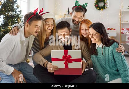Heureux amis se réunissant autour de maté ouvrant la boîte cadeau, célébrant Noël et échangeant des cadeaux. Banque D'Images