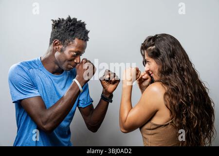 Un jeune couple diversifié se tient dans une position de combat ludique mais déterminée, prêt à espar. Un concept de concurrence, de partenariat, face aux défis Banque D'Images