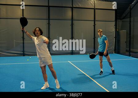 Deux jeunes hommes démontrent leurs compétences tout en jouant au padel avec des raquettes sur le court. Banque D'Images