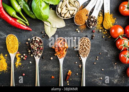 cuillères avec différentes épices et légumes sur une table noire Banque D'Images