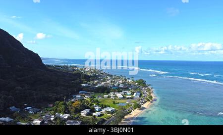 Vue aérienne d'une ville côtière hawaïenne avec océan turquoise, plage de sable et montagnes luxuriantes. Banque D'Images