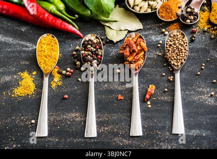 cuillères avec différentes épices et légumes sur une table noire Banque D'Images