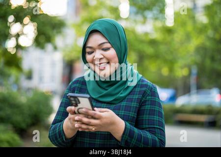 Portrait d'une jeune femme musulmane utilisant un téléphone portable à l'extérieur Banque D'Images