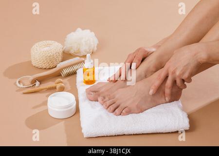 Femme pieds sur une serviette entourée de produits cosmétiques, brosse, crème et huile pour une routine beauté de soin des pieds. Concept d'auto-soins, de spa et de santé de la peau. Banque D'Images