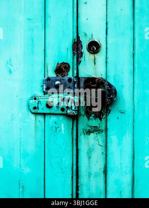Une vieille porte de couleur sarcelle, vieillie par les intempéries, avec une serrure et des charnières rouillées. Banque D'Images