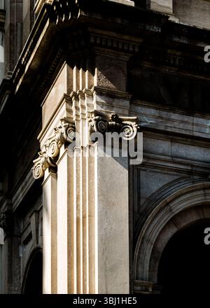 Gros plan du coin d'un bâtiment, présentant des détails architecturaux tels que des colonnes, des chapiteaux ornés et une entrée voûtée. Le jeu de lumière Banque D'Images