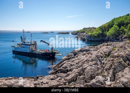 Petit navire côtier amarré le long d'un rivage rocheux sous un ciel dégagé à l'extérieur d'Egersund, Rogaland, Norvège, le 14 juillet 2018 Banque D'Images