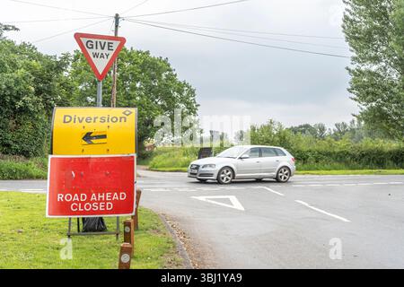Vue rapprochée d'une route devant un panneau fermé, avec un panneau fléché de déviation. Banque D'Images