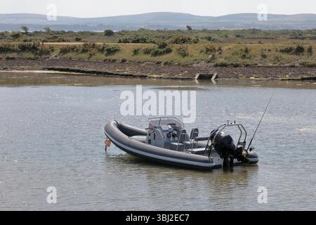 Un bateau gonflable rigide motorisé gris amarré dans l'eau avec de l'herbe et des buissons derrière et des vues lointaines de l'île de Wight en arrière-plan Banque D'Images