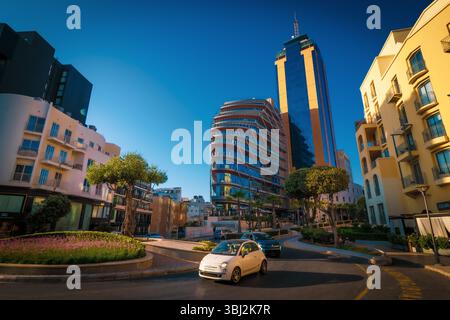 Vue panoramique d'une voiture blanche Fiat 500 circulant autour d'un rond-point devant la Tour d'affaires Portomaso à Saint Julian's (San Ġiljan), Malte Banque D'Images