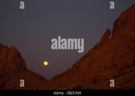 Une pleine lune jaune se couche derrière le Spitzkoppe, en Namibie. Banque D'Images