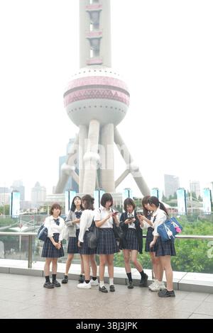 Au début de l'été à Shanghai, près du Bund, des lycéennes japonaises en uniforme se rassemblent devant la Tour de la Perle orientale, leur présence s'ajoutant Banque D'Images