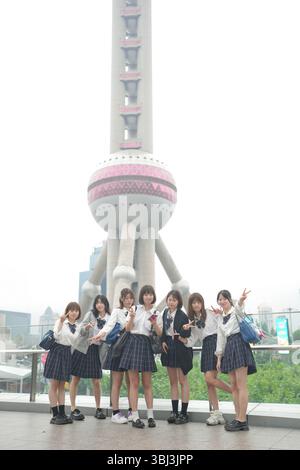Au début de l'été à Shanghai, près du Bund, des lycéennes japonaises en uniforme prennent une photo de groupe devant la Tour de la Perle orientale, leur smil Banque D'Images