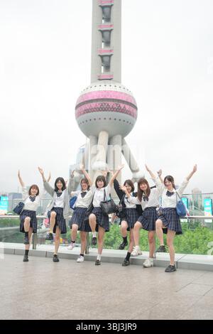 Au début de l'été à Shanghai, près du Bund, des lycéennes japonaises en uniforme prennent une photo de groupe devant la Tour de la Perle orientale, leur smil Banque D'Images