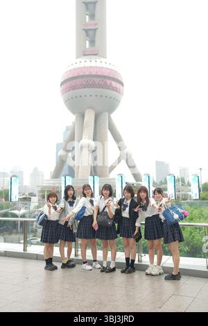 Au début de l'été à Shanghai, près du Bund, des lycéennes japonaises en uniforme prennent une photo de groupe devant la Tour de la Perle orientale, leur smil Banque D'Images