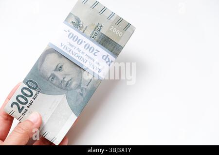 Pekanbaru, Indonésie - 21 mars 2025 : main tenant des billets de banque rupiah indonésiens RP 2,000 isolés sur fond blanc pour THR sur Eid al-Fitr ou Lebara Banque D'Images