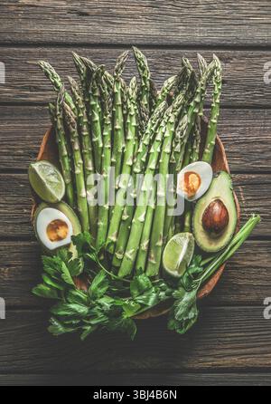 Bouquet d'asperges vertes avec demi-œufs, avocat, persil et citron vert sur une table de cuisine rustique en forme de bois. Préparation saine de la cuisine à la maison avec spri saisonnier Banque D'Images