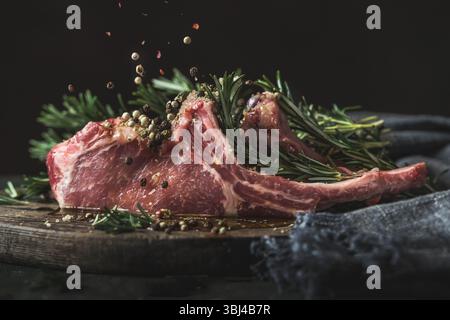 Gros plan sur les porte-porc ibérique avec des épices en chute : poivre au romarin sur fond sombre. Délicieuse viande fraîche pour barbecue avec de l'assaisonnement savoureux Banque D'Images