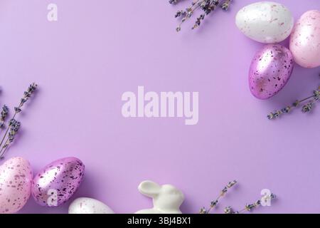 Belle composition de Pâques avec des œufs mouchetés pastel, des brins de lavande et un lapin en céramique sur fond violet. Banque D'Images
