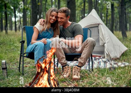 Un couple aimant câlin par un feu de camp, profitant de l'atmosphère tranquille d'une soirée paisible dans la nature, savourant leur romance et l'excitation de Banque D'Images