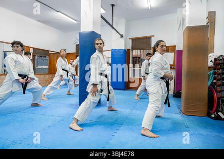 Groupe de karatéka s'exerçant ensemble dans un dojo, portant un keikogi blanc et des ceintures noires Banque D'Images